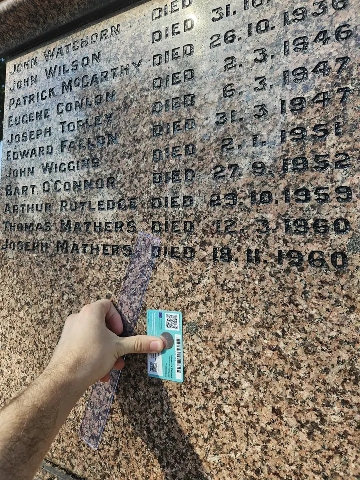 A gravestone photographed from a strong side angle, making the card and lettering recede