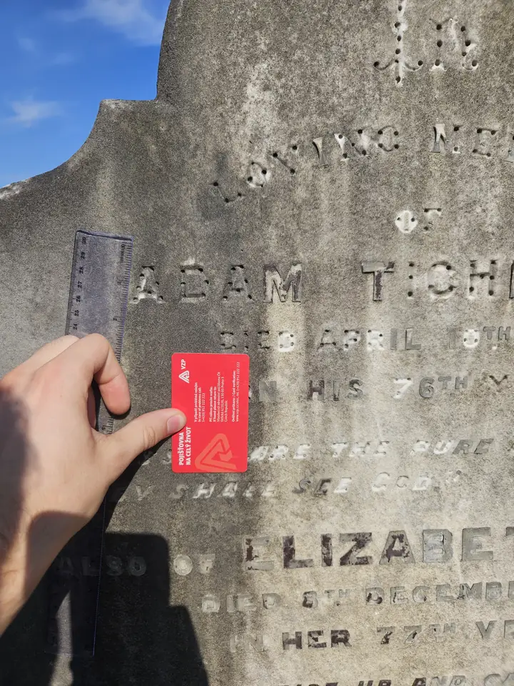 A card held flat while the camera faces the gravestone nearly square-on