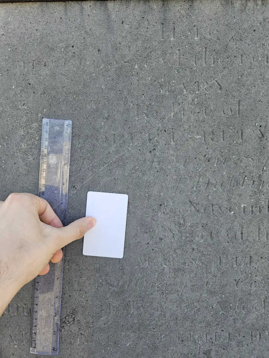 A bank card pressed flat against a gravestone with one thumb while all four card corners remain visible